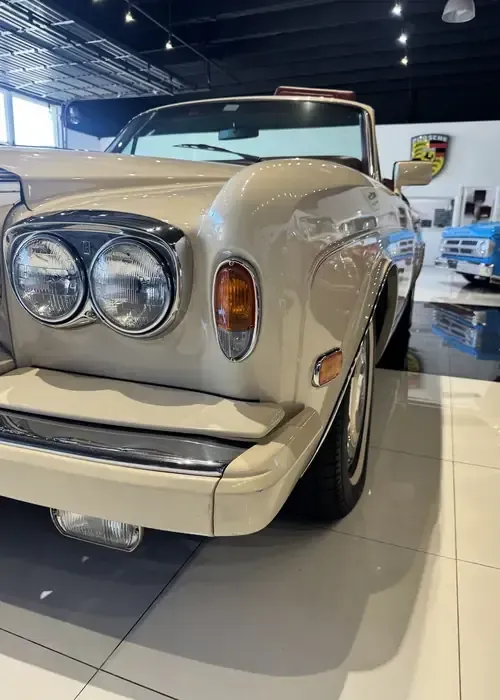 Cream-colored classic car with twin round headlights displayed indoors on a showroom floor