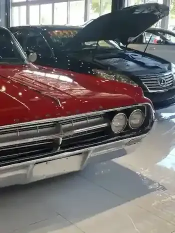 Classic red car with chrome grille displayed indoors beside a black car with its hood open