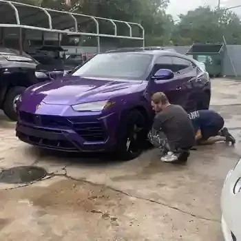 Two people crouch by the front wheel of a purple SUV in a parking lot.