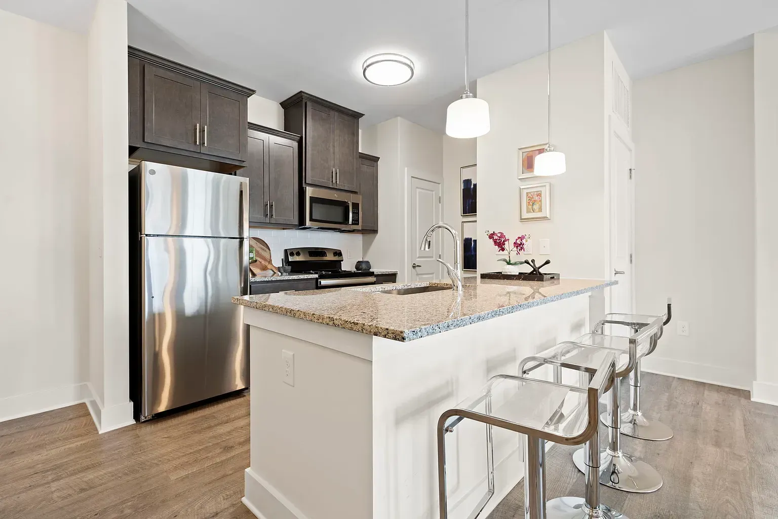 Modern apartment kitchen with granite island, stainless steel appliances, and bar stools.