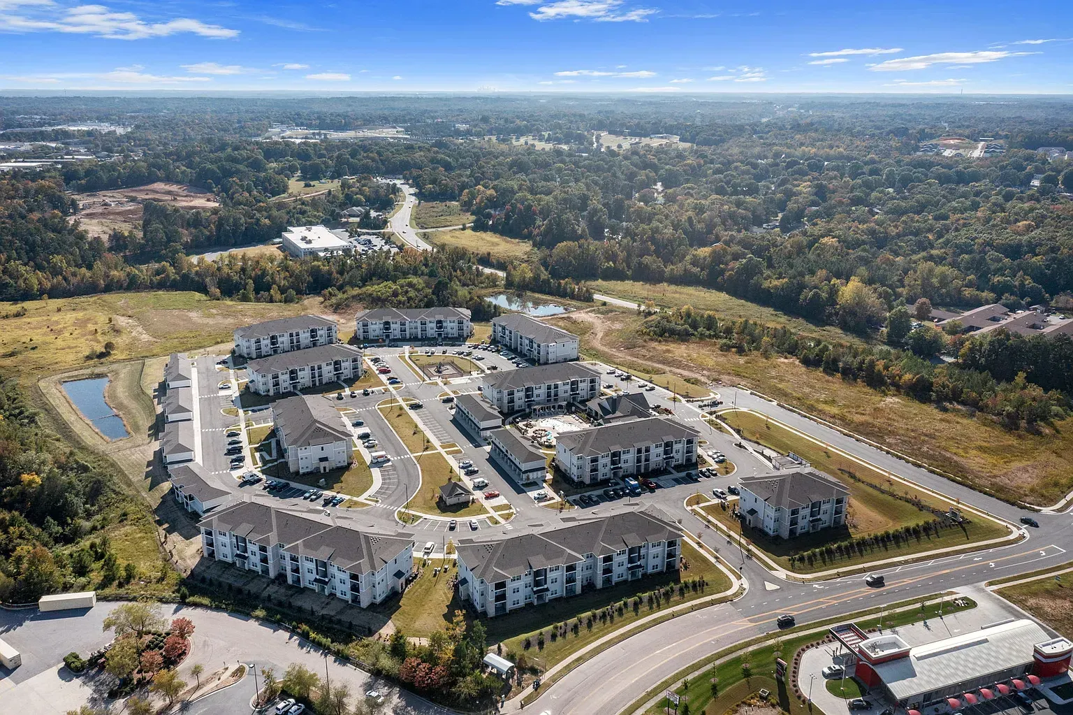 Aerial view of a multi-building apartment community with parking lots and surrounding trees.