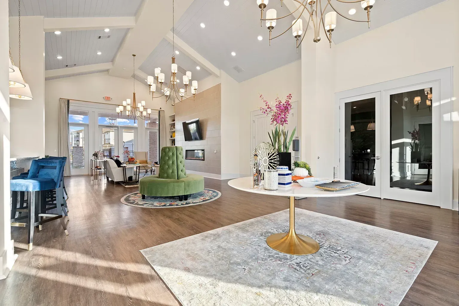 Bright community lounge with seating, chandeliers, and glass doors.