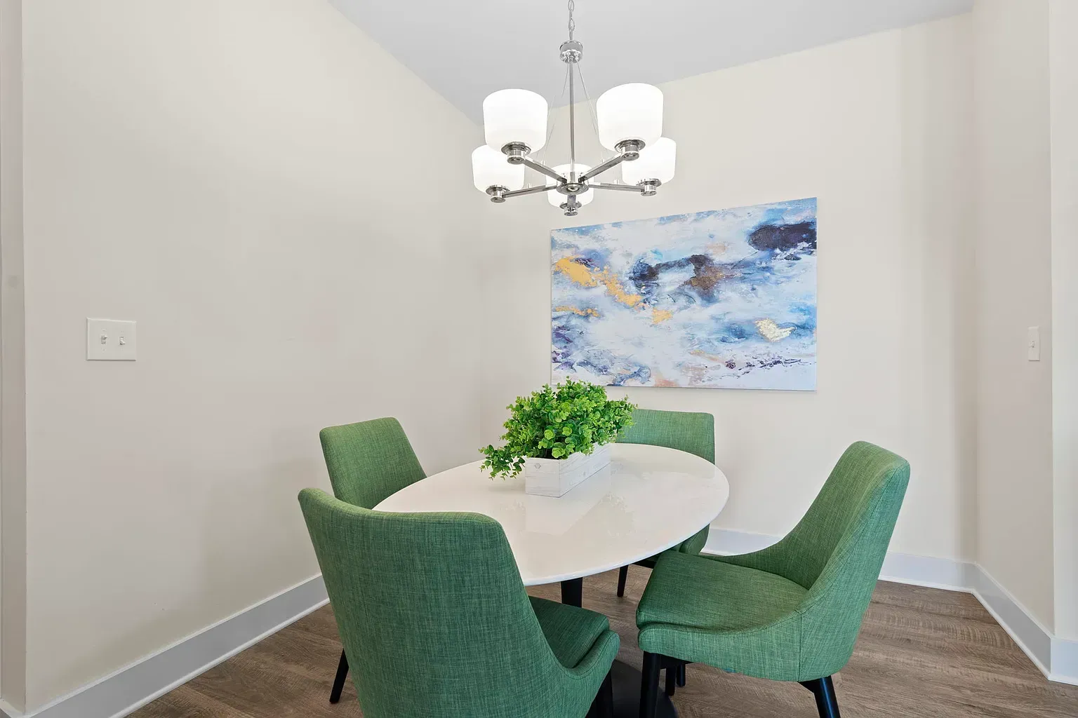 Dining nook with a white round table, four green upholstered chairs, and a modern chandelier.