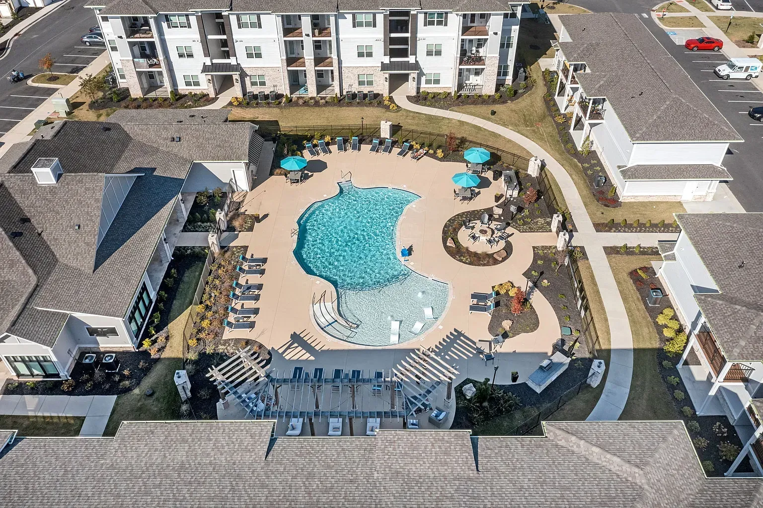 Aerial view of a residential community pool with loungers, umbrellas, and surrounding apartment buildings.