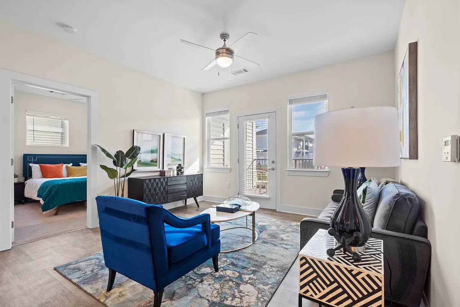 Bright living room in an apartment with a blue accent chair, gray sofa, and doorway to bedroom.