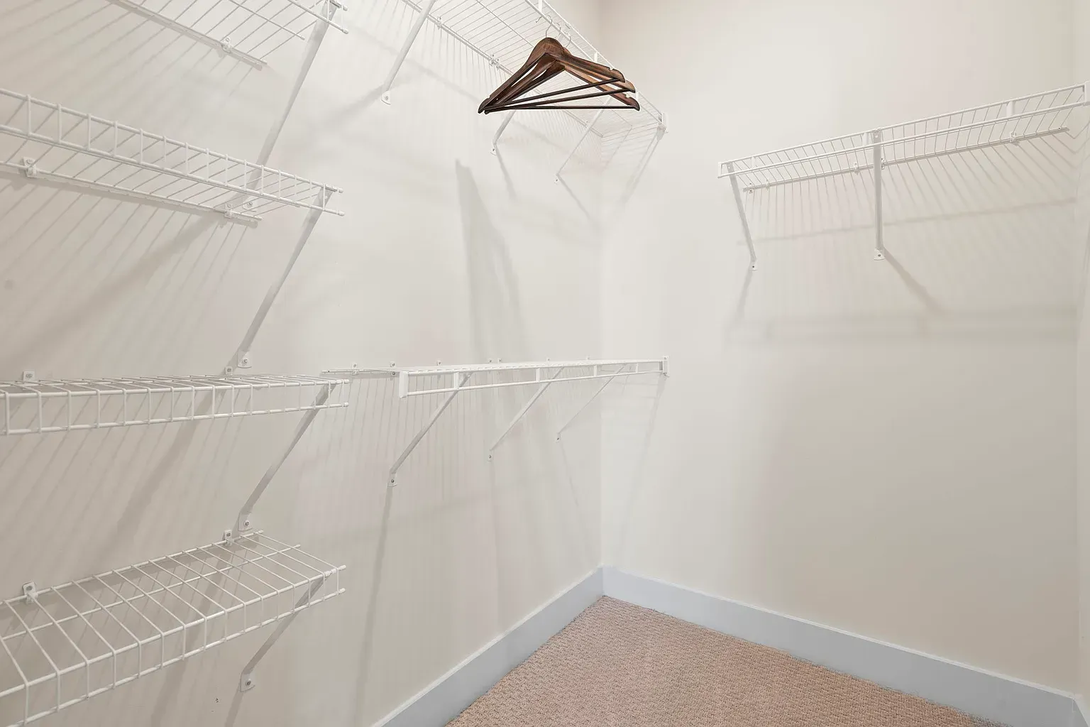 Walk-in closet with white wire shelving and hanging rods, beige carpet.