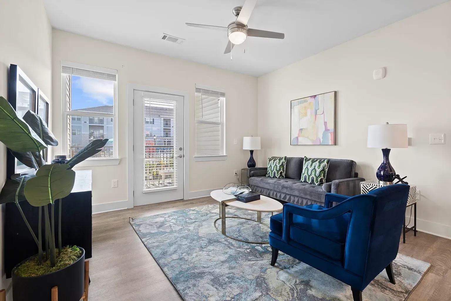 Living room in an apartment with a gray sofa, blue chair, coffee table, rug, and ceiling fan.