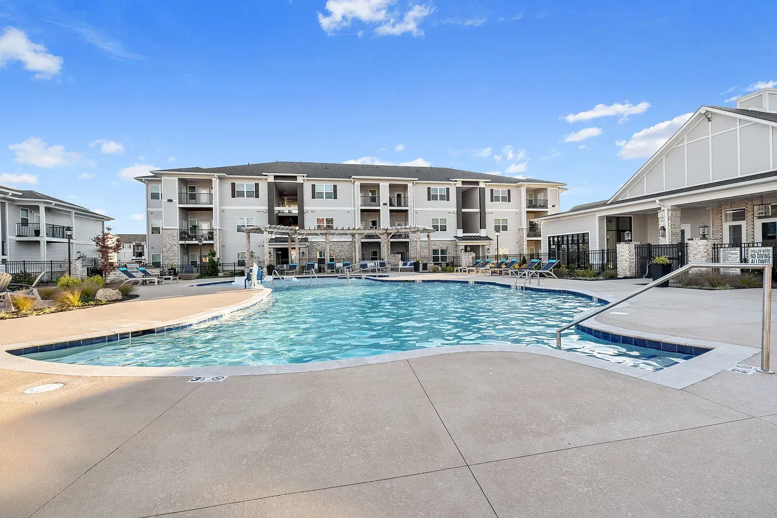 Outdoor apartment community pool with lounge chairs and a pergola, building in the background.