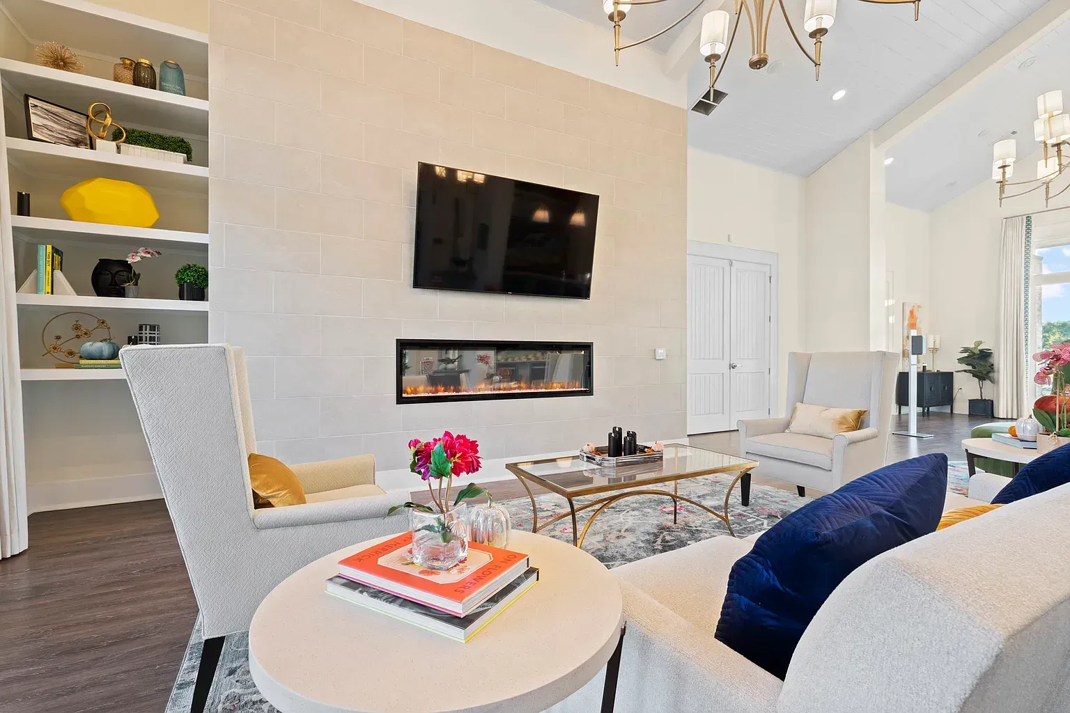 Bright living room with a wall-mounted TV above a linear fireplace, white seating, and built-in shelves.