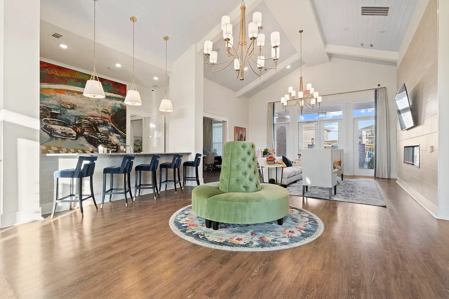 Bright modern lounge with a bar, seating, chandeliers, and a wall-mounted TV.