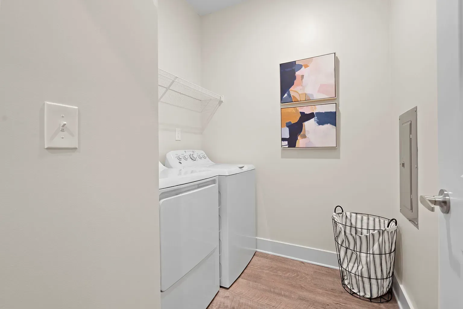 Laundry room with a washer and dryer, wire shelf, and a striped laundry basket.