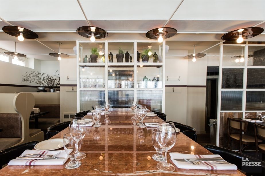 A long table in a restaurant with glasses and napkins on it.