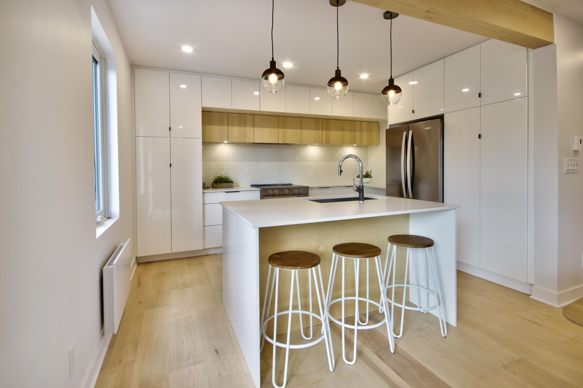 A kitchen with white cabinets , a large island , stools and a refrigerator.