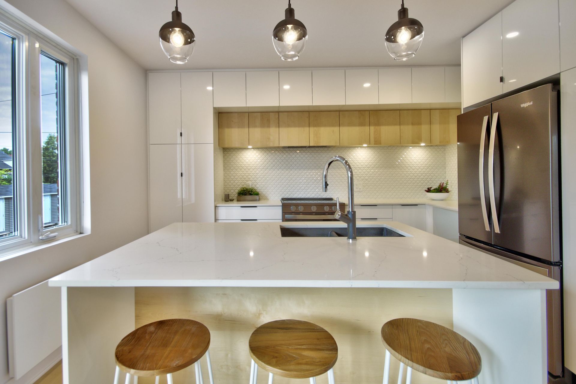 A kitchen with a large island , stools , a refrigerator and a sink.