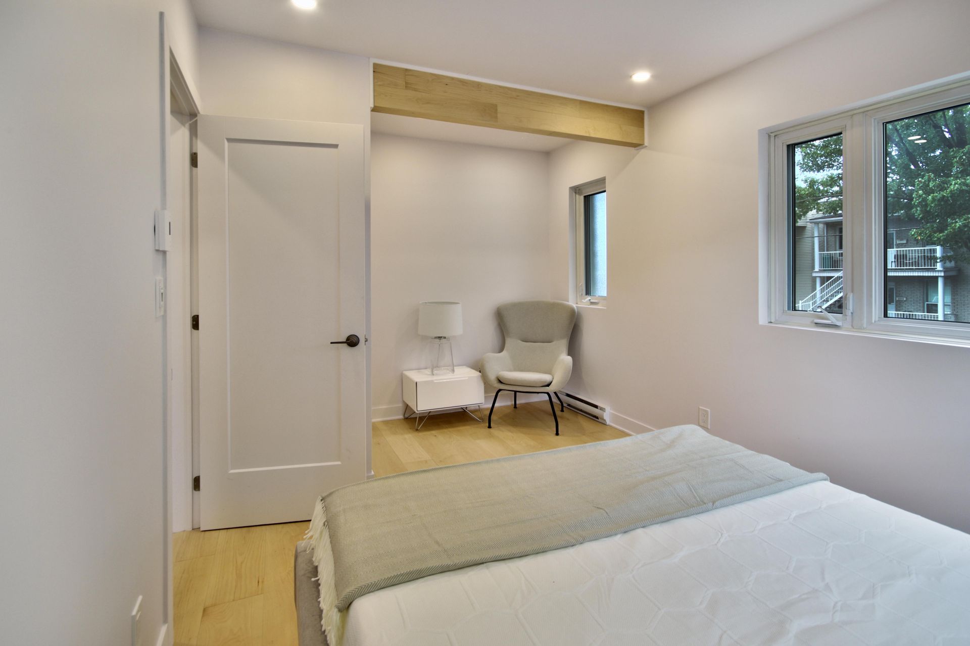 A bedroom with a bed , chair , nightstand and window.