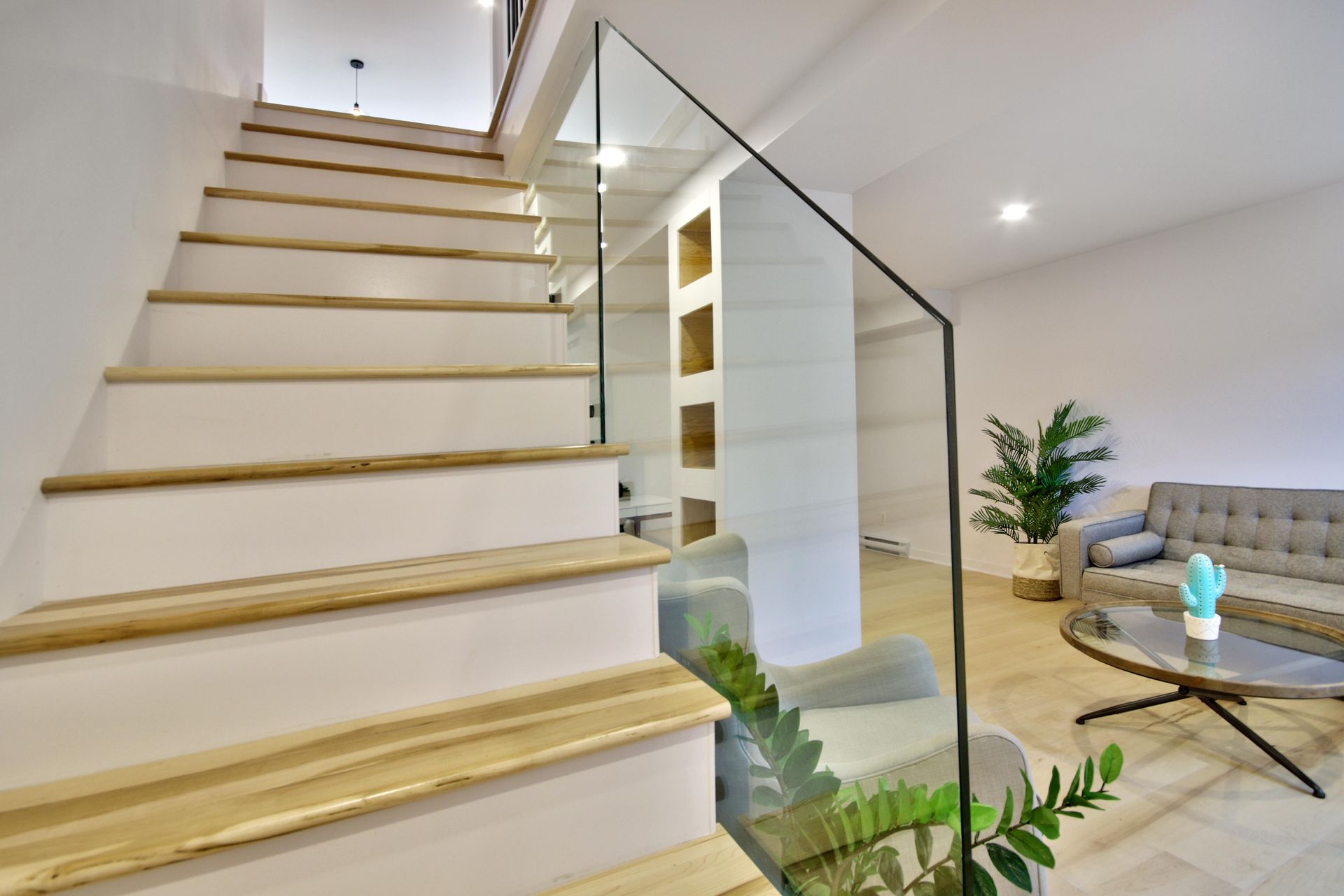 A living room with stairs leading up to the second floor and a glass railing.