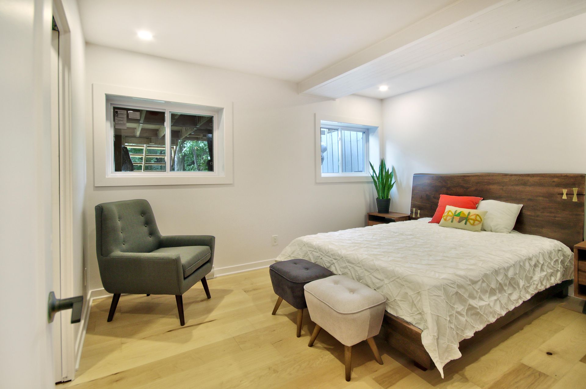 A bedroom with a bed , chair , ottoman and window.