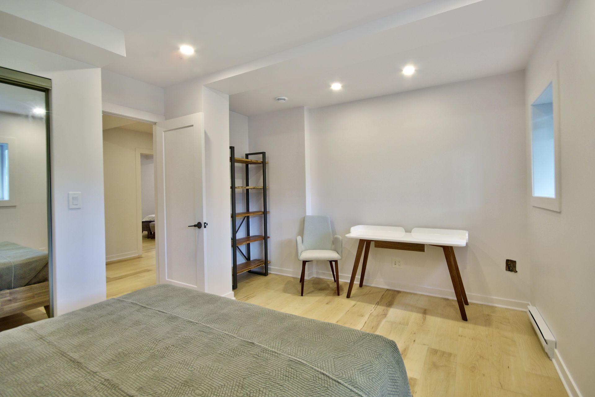 A bedroom with a bed , desk , chair and mirror.