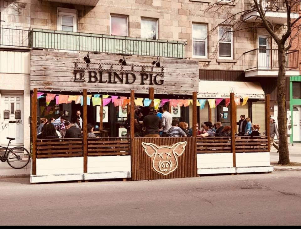 A group of people are sitting outside of a restaurant called the blind pig.