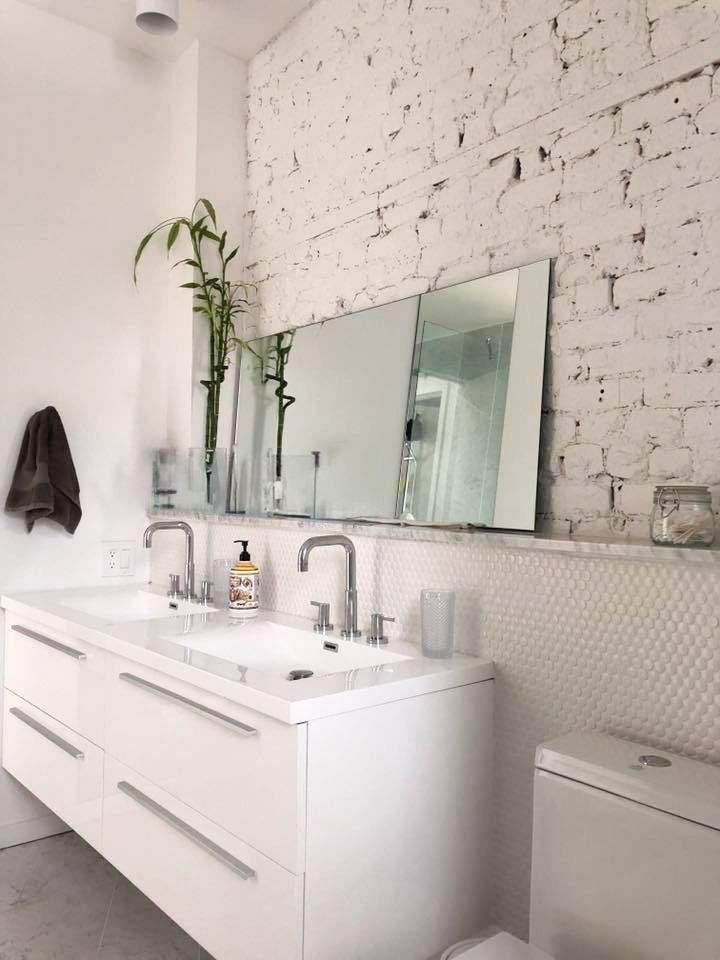 A bathroom with two sinks and a toilet with a white brick wall