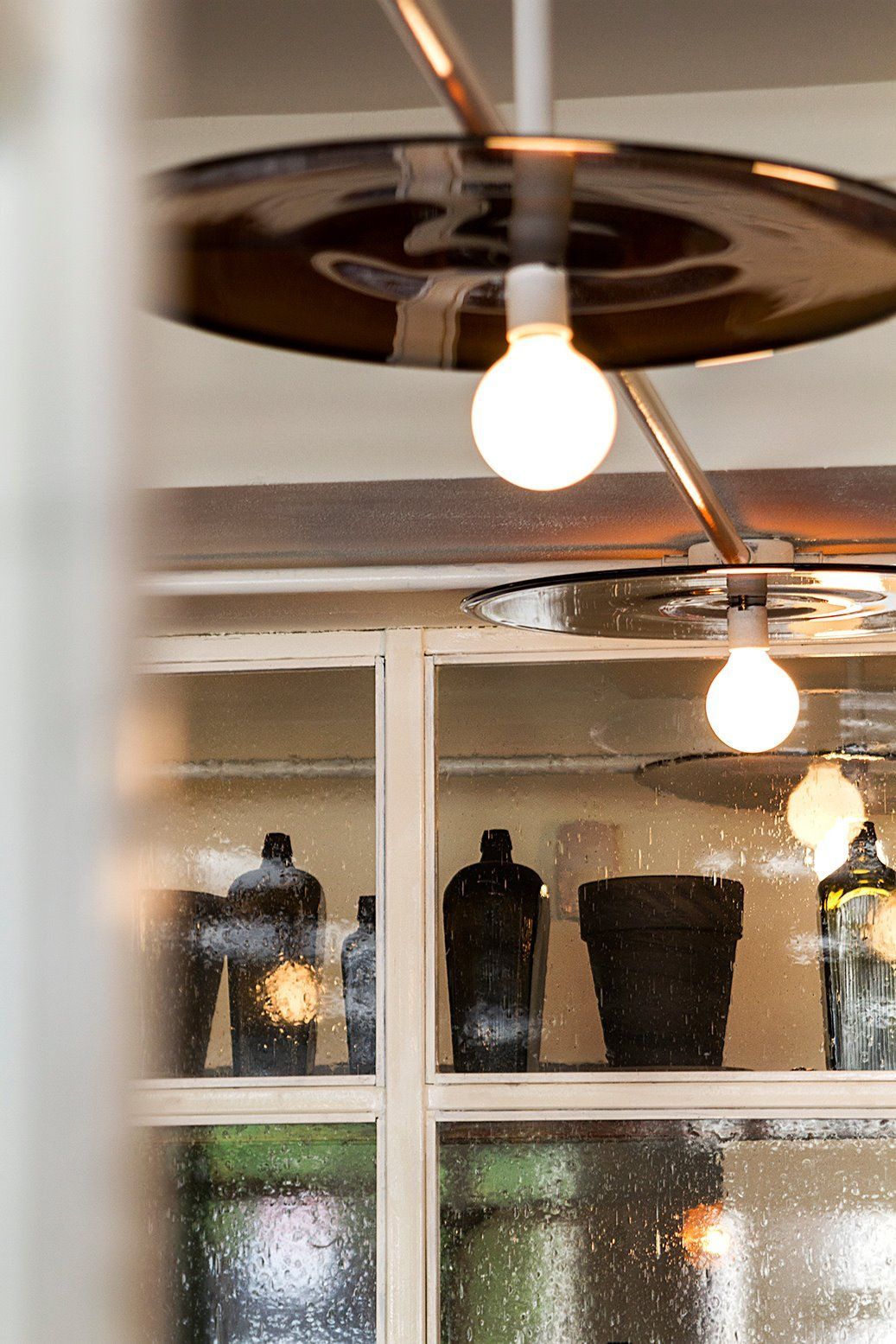 A light bulb is hanging from the ceiling above a glass shelf with bottles on it.