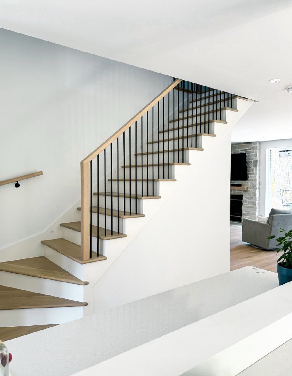 A white staircase with wooden steps and a black railing in a living room.