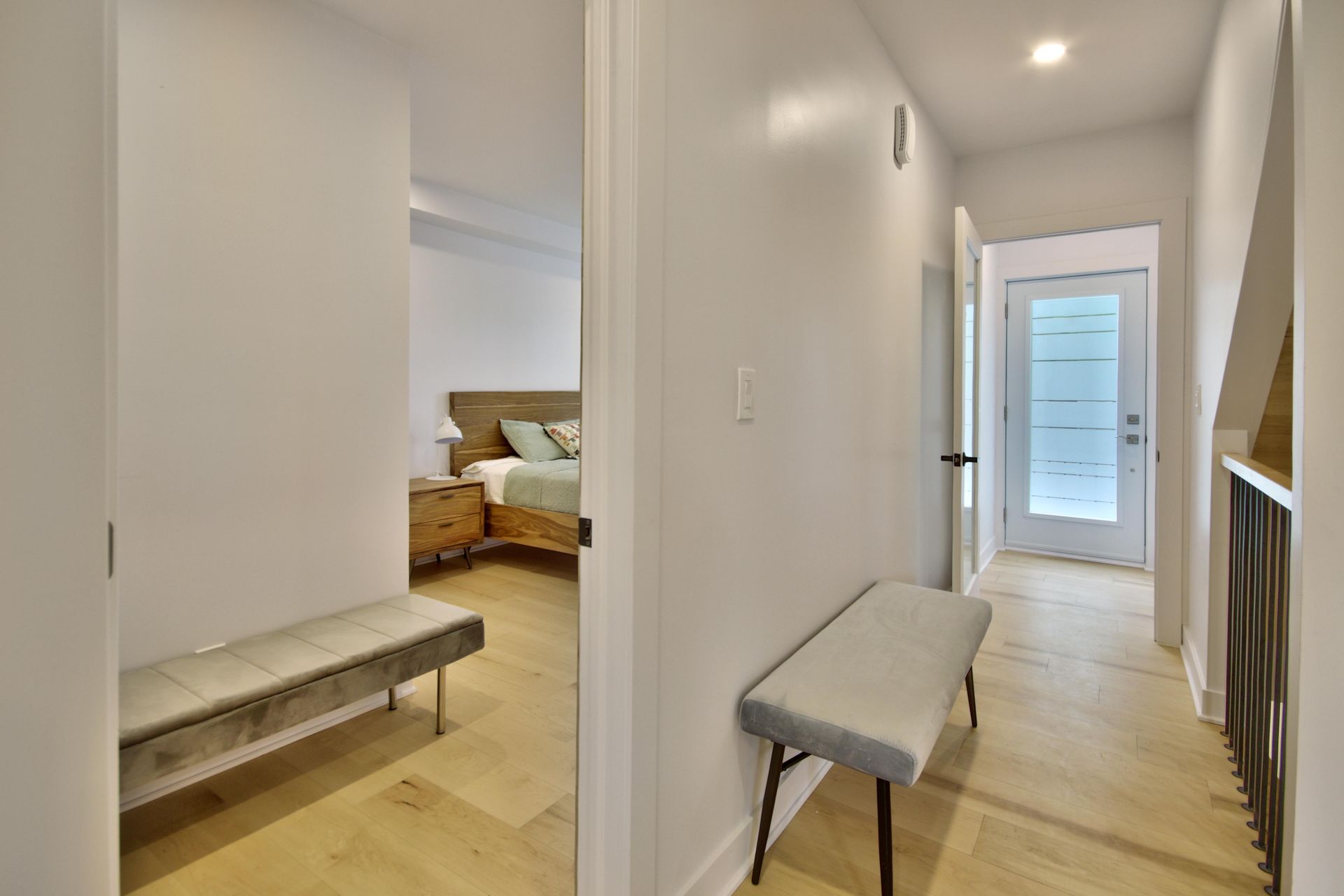 A hallway with a bench and a bed in the background.