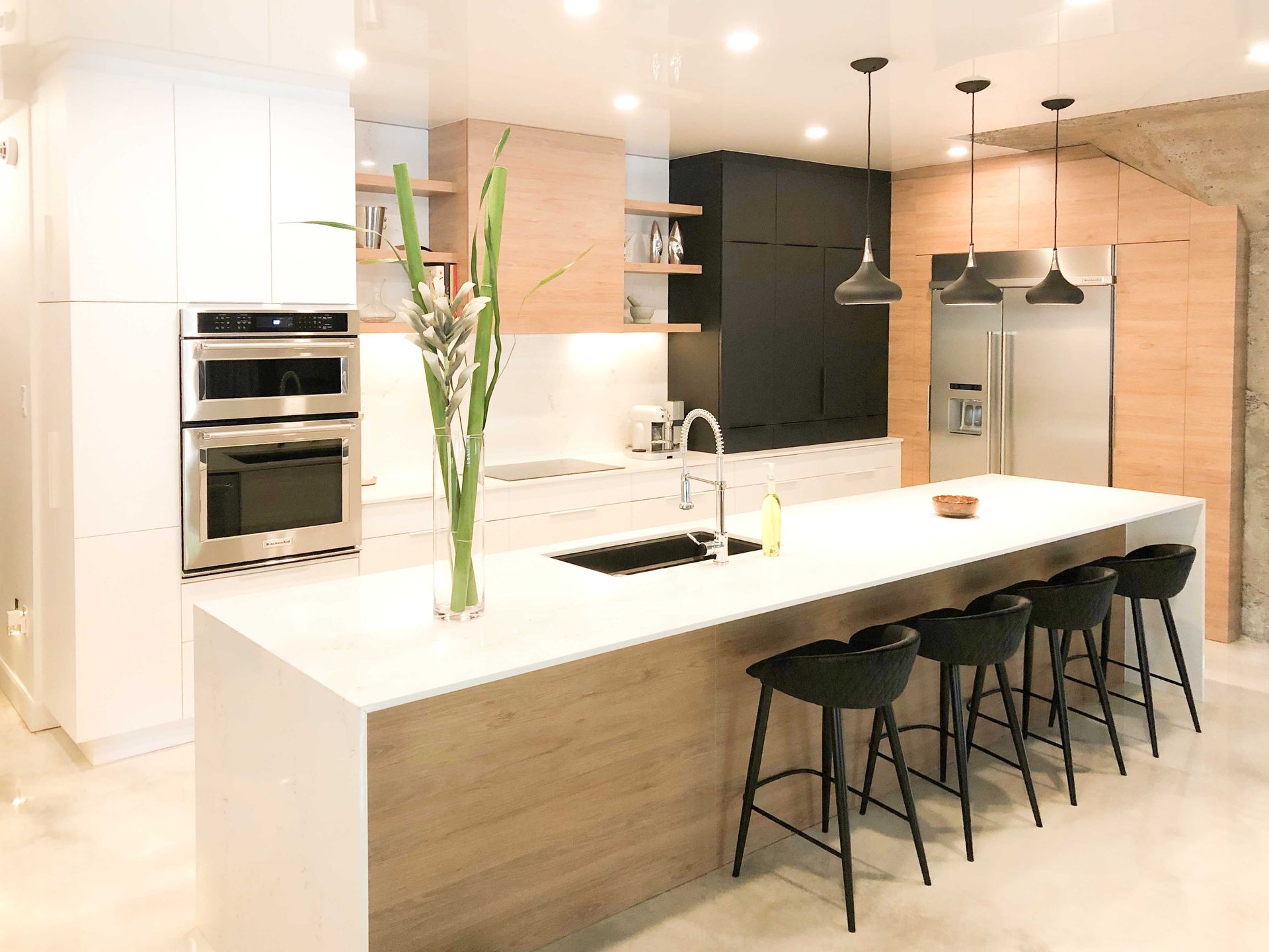 A kitchen with a large island and stools and a vase of flowers on the counter.