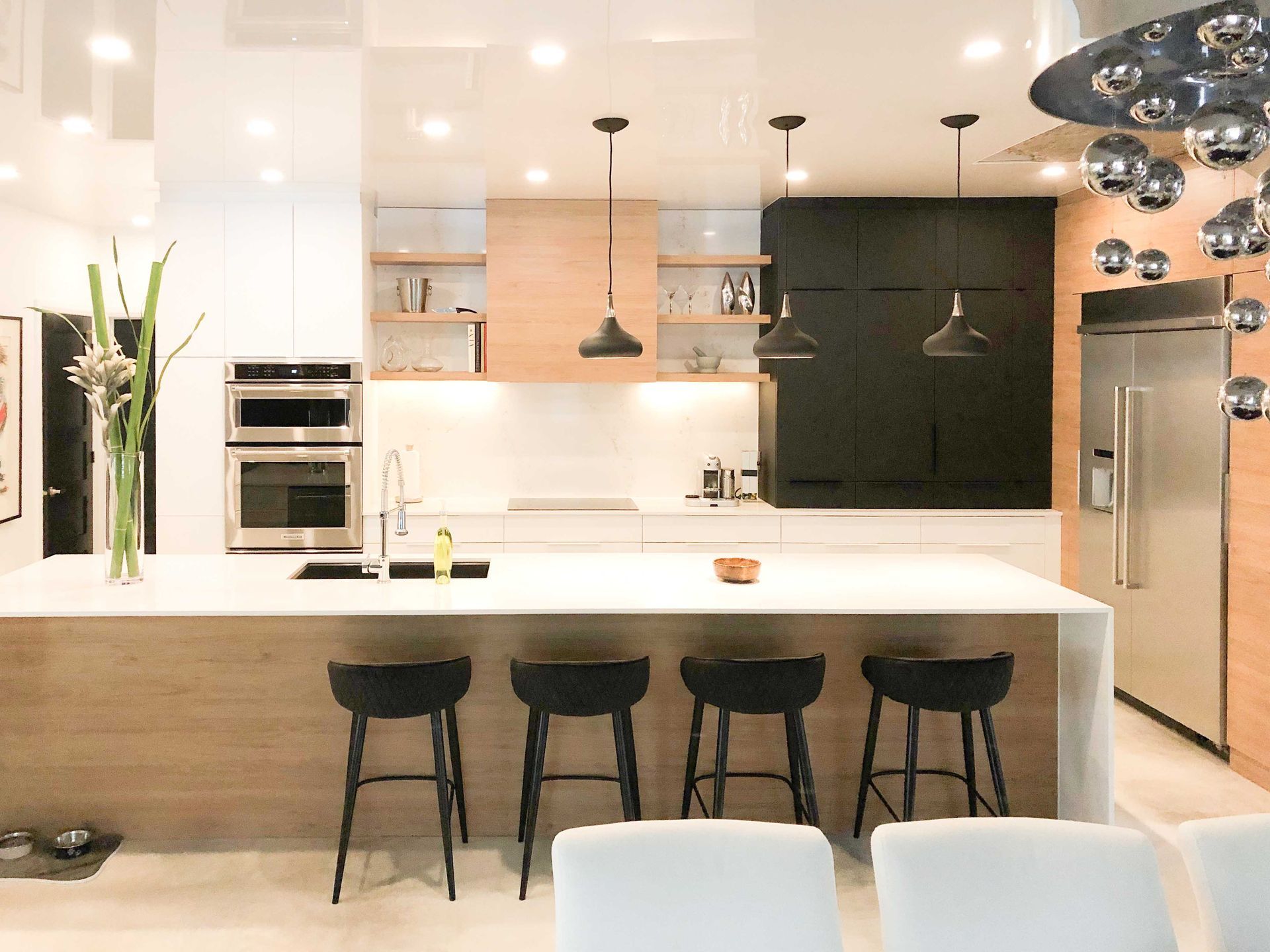 A kitchen with a large island , stools and a refrigerator.