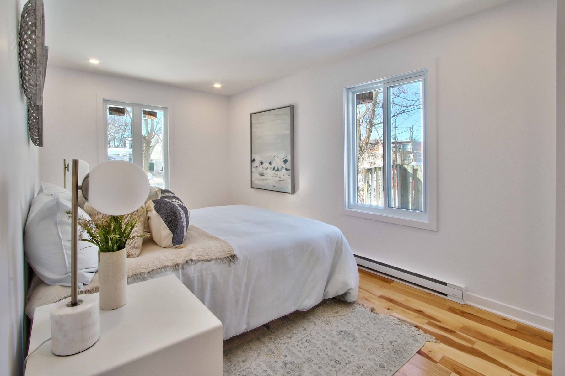 A bedroom with a bed , nightstand , lamp and window.