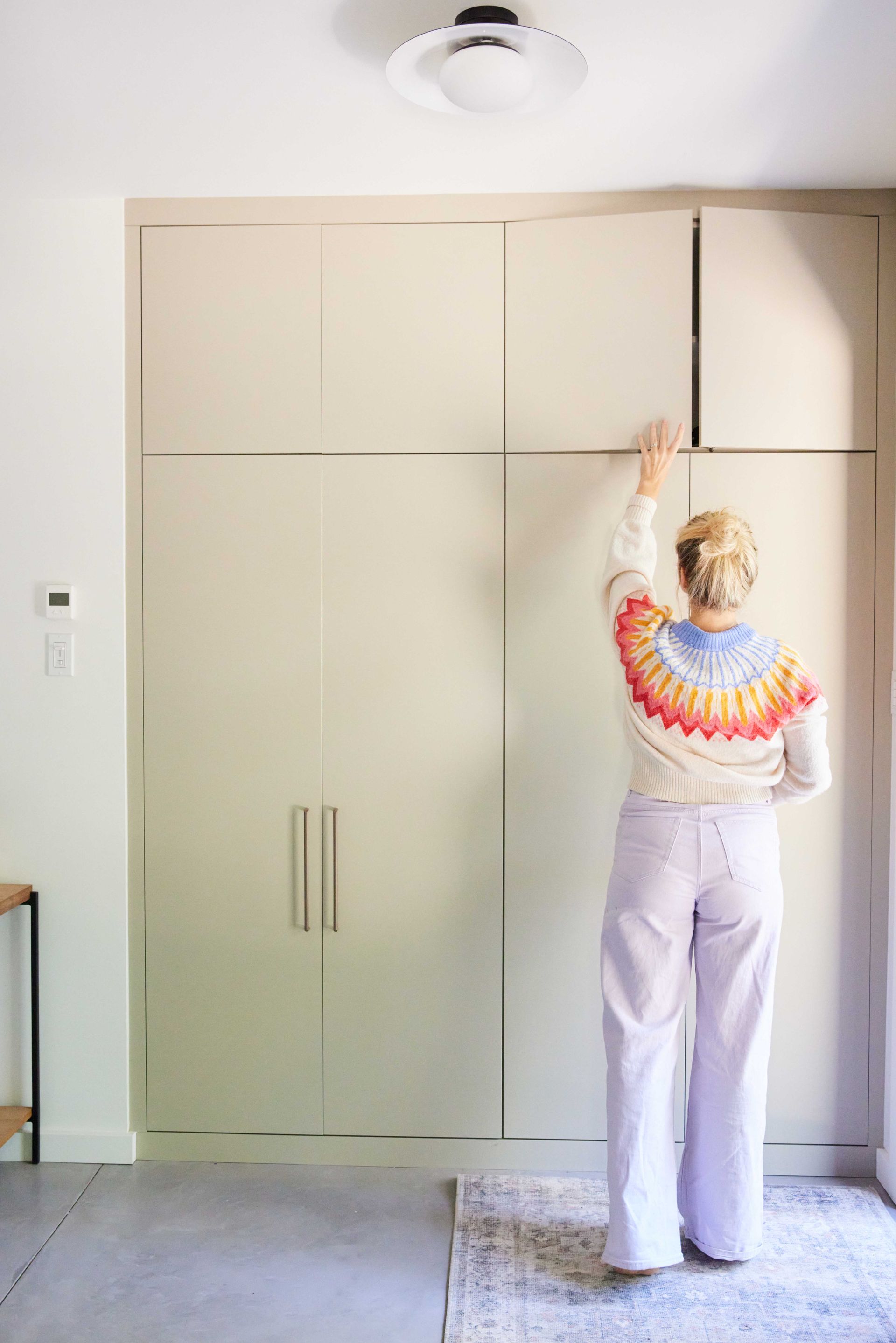 A woman in a colorful sweater is standing in front of a white cabinet.