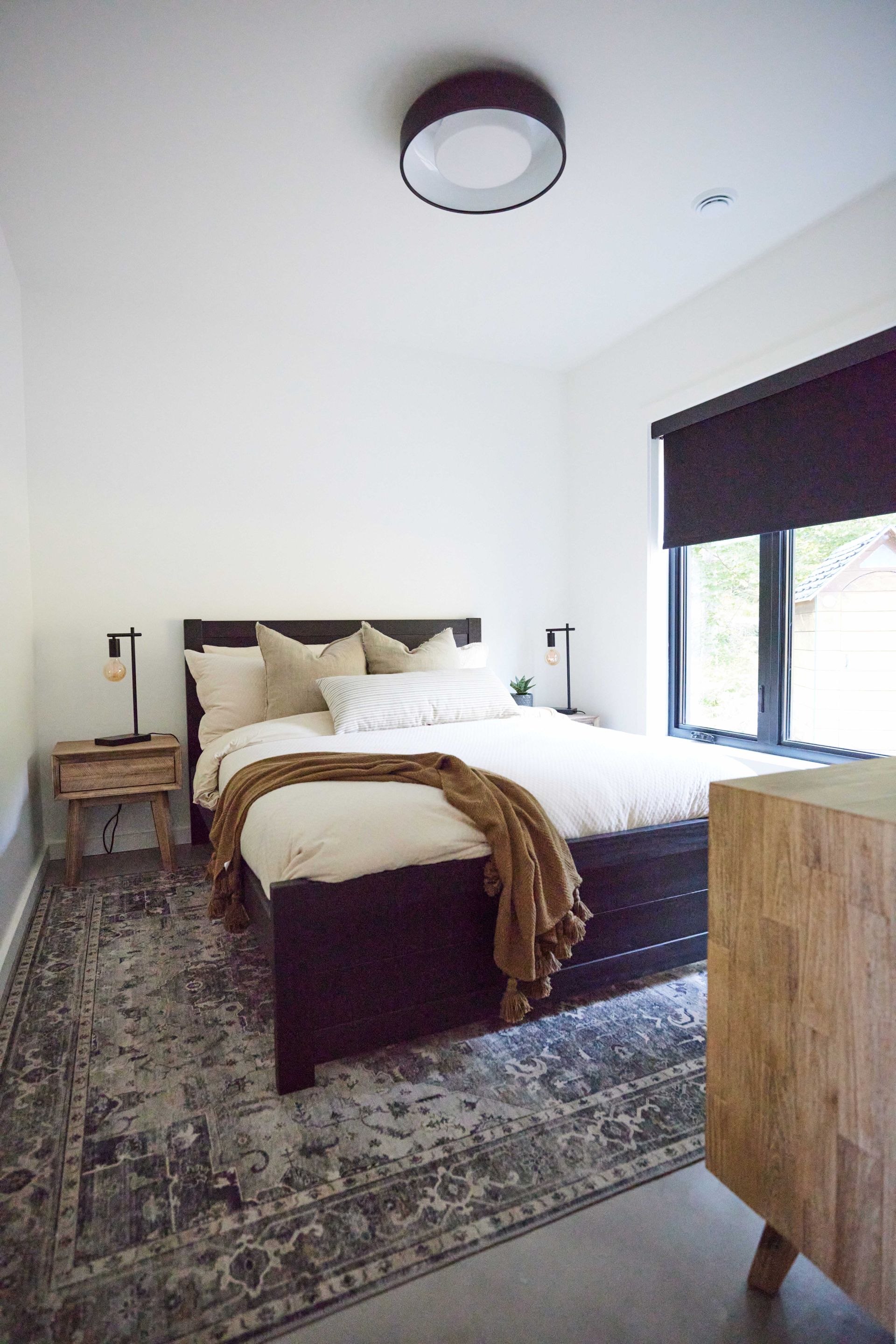 A bedroom with a bed , nightstand , rug and window.