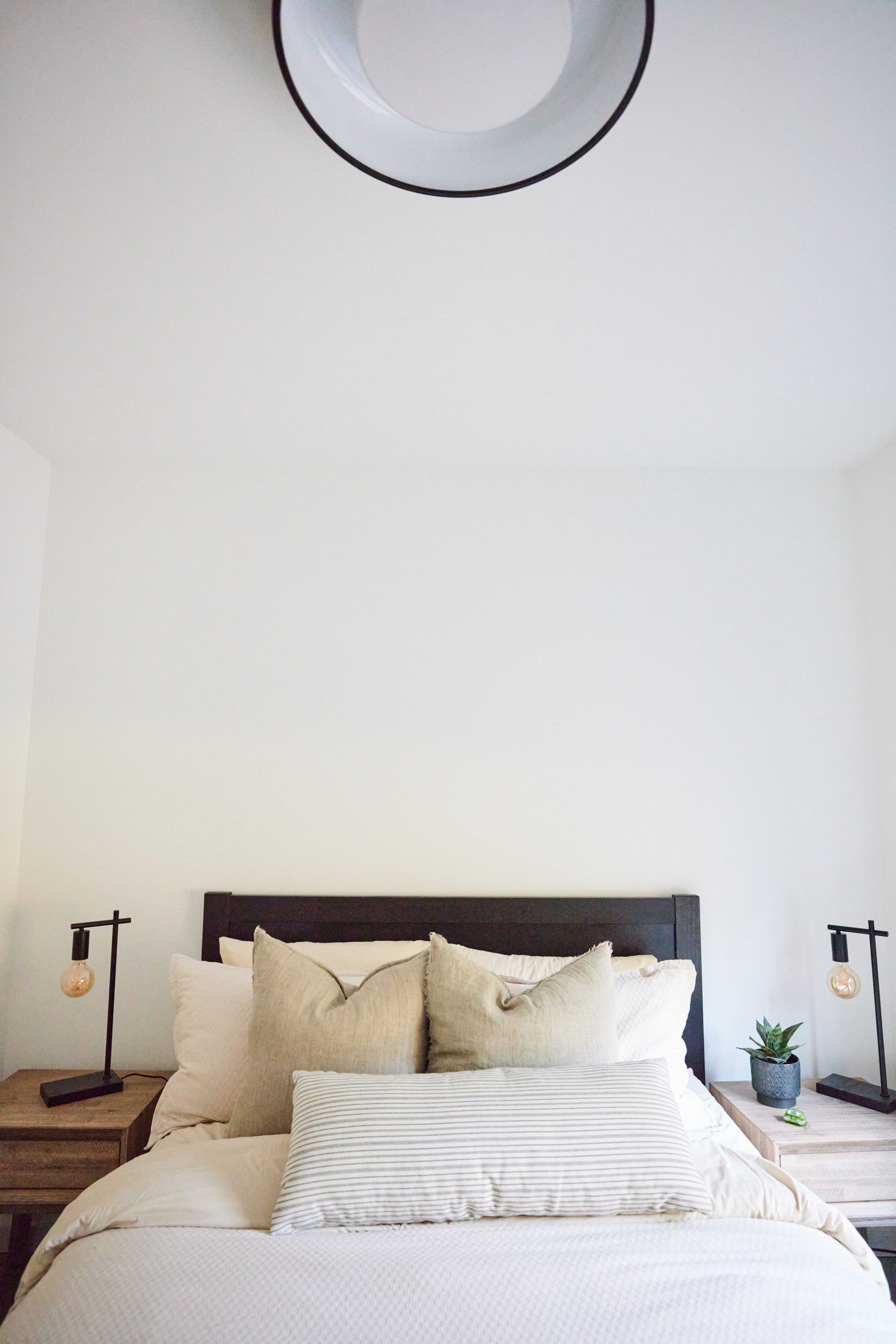 A bed with white sheets and pillows in a bedroom with a white wall.