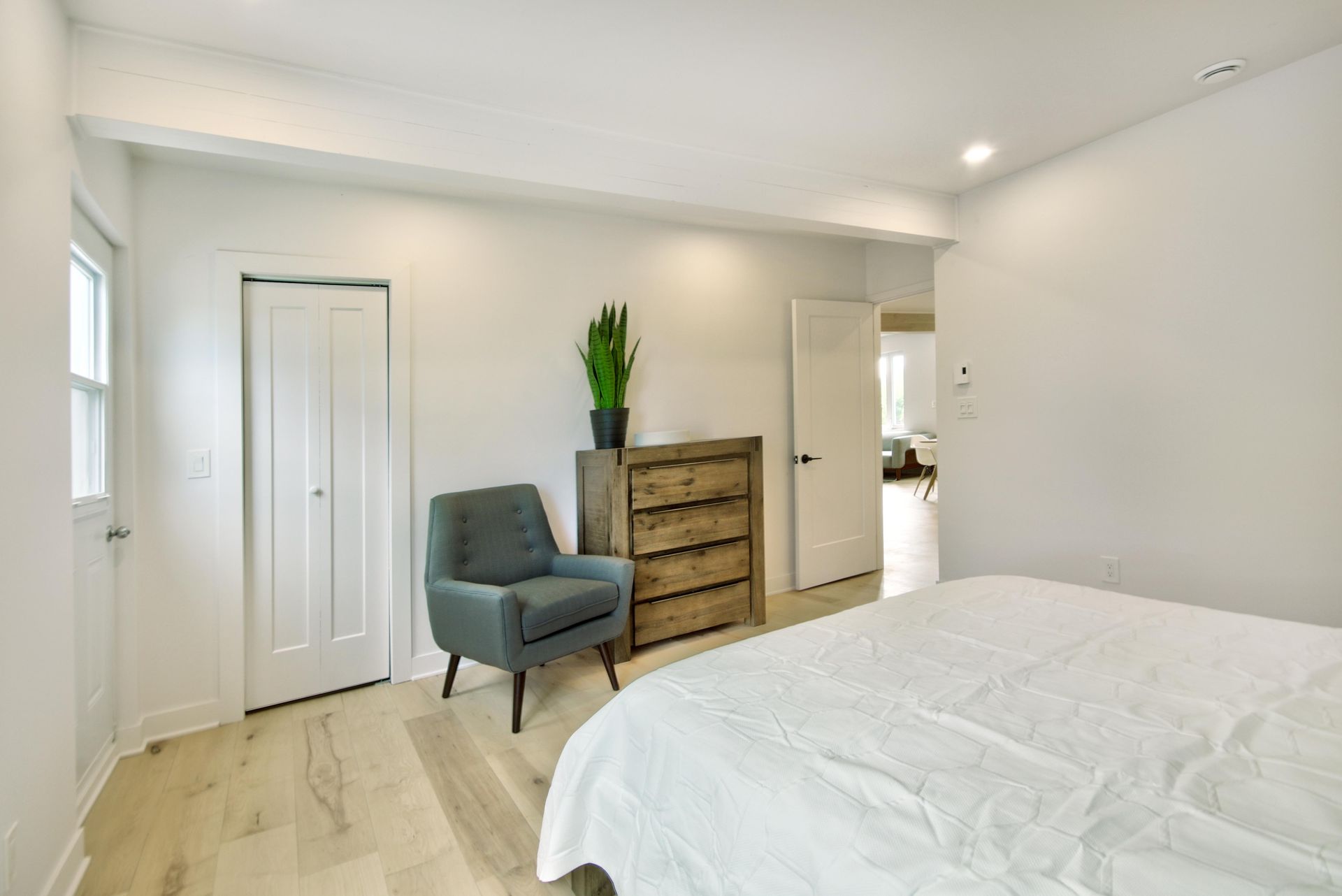 A bedroom with a bed , chair , dresser and window.