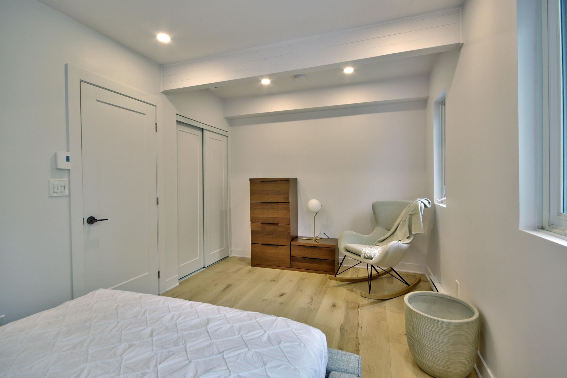 A bedroom with a bed , chair , dresser and window.