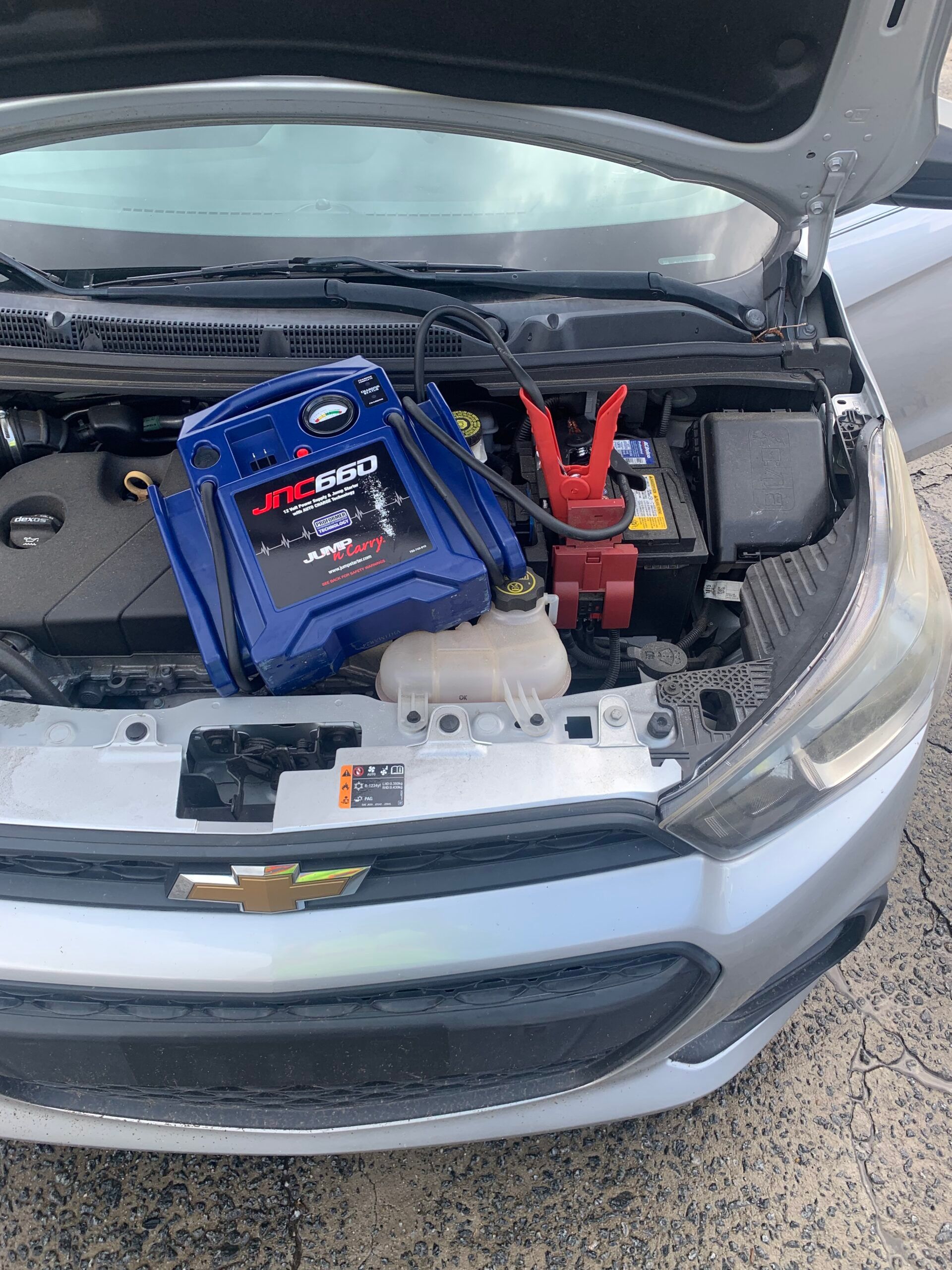 A car with the hood open and a jump starter in the engine compartment.