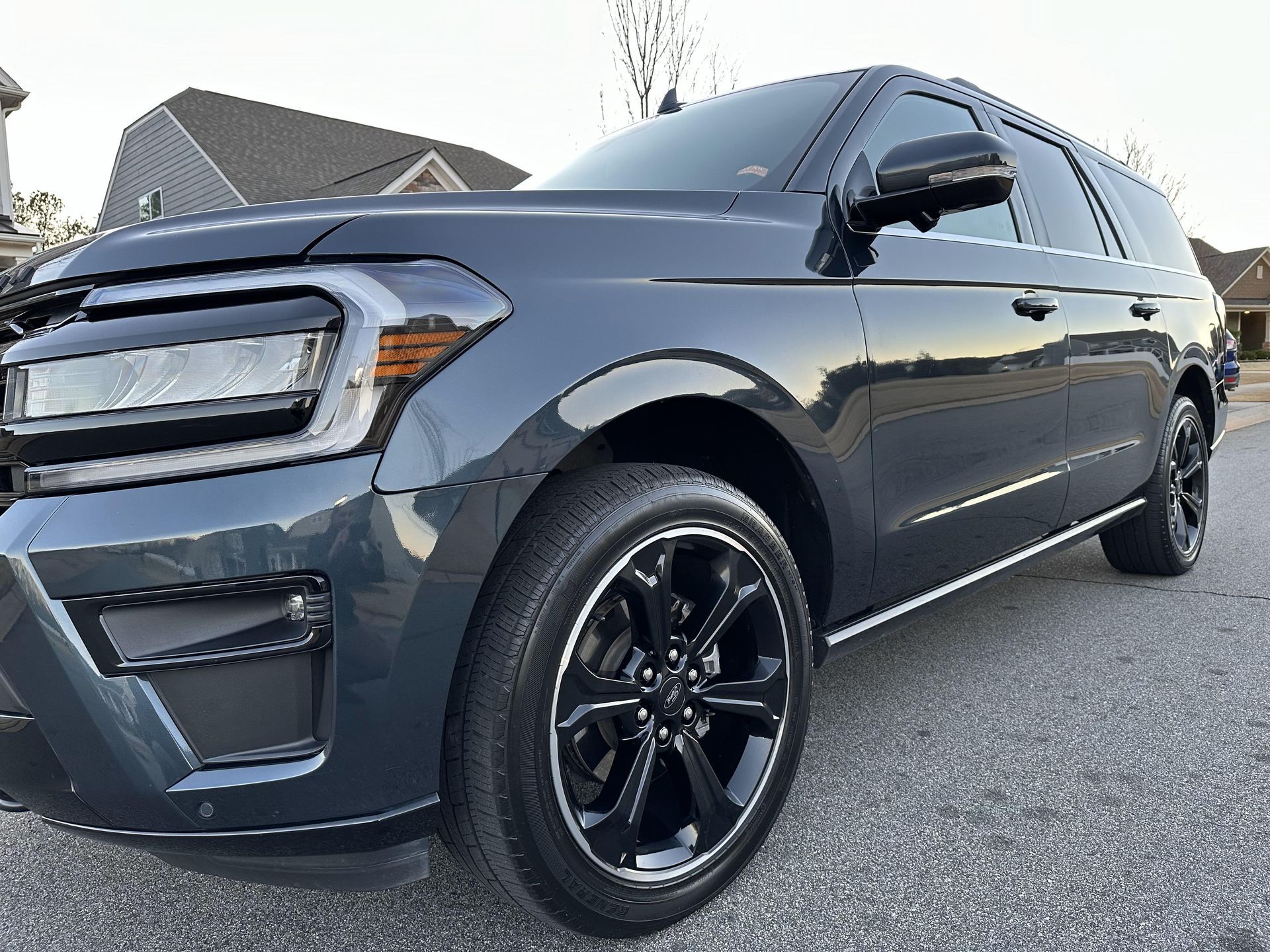 A black ford expedition is parked on the side of the road in front of a house.
