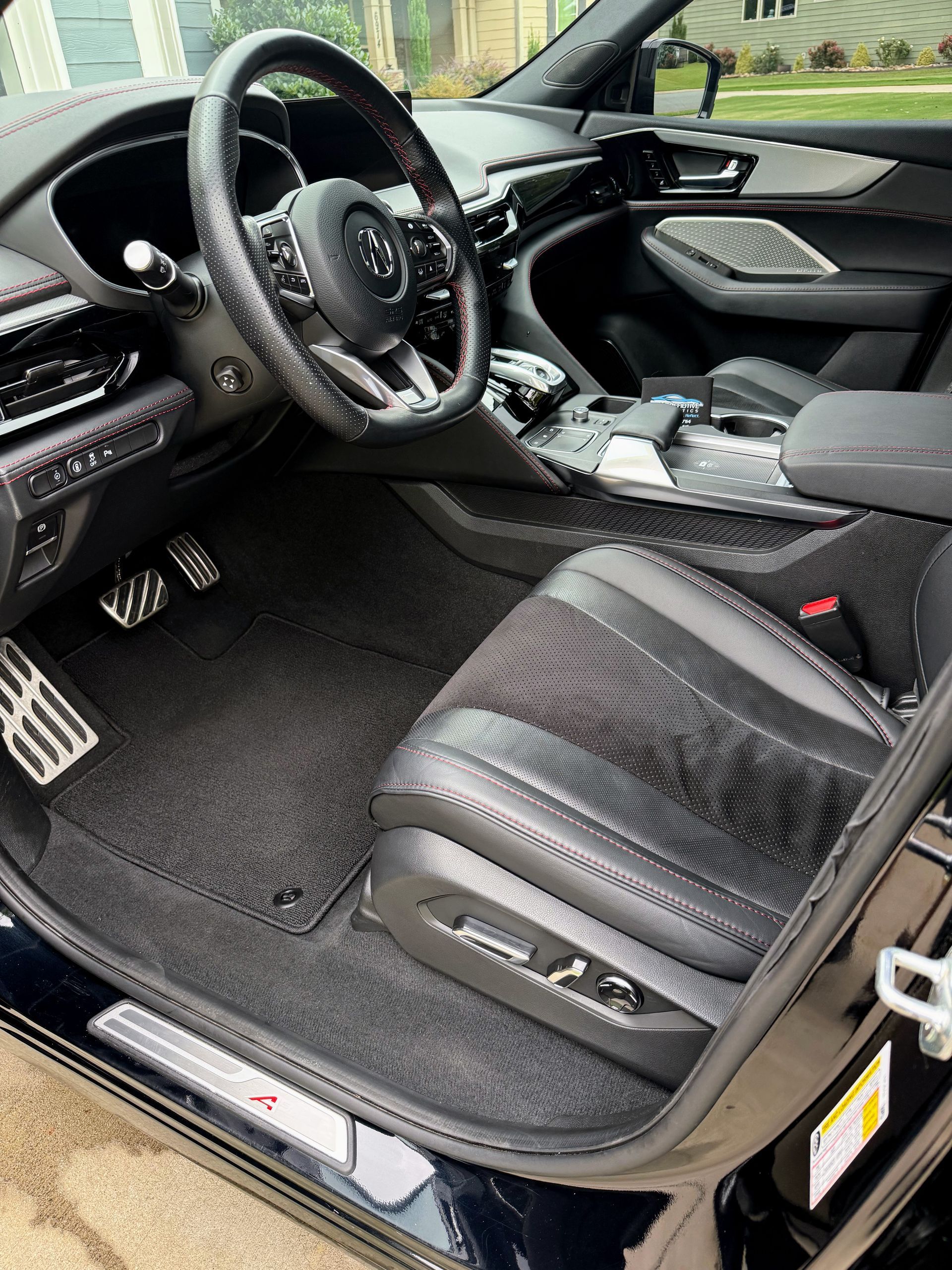 Black Acura MDX interior with black and red accents, showing driver's seat, steering wheel, and floor mats.