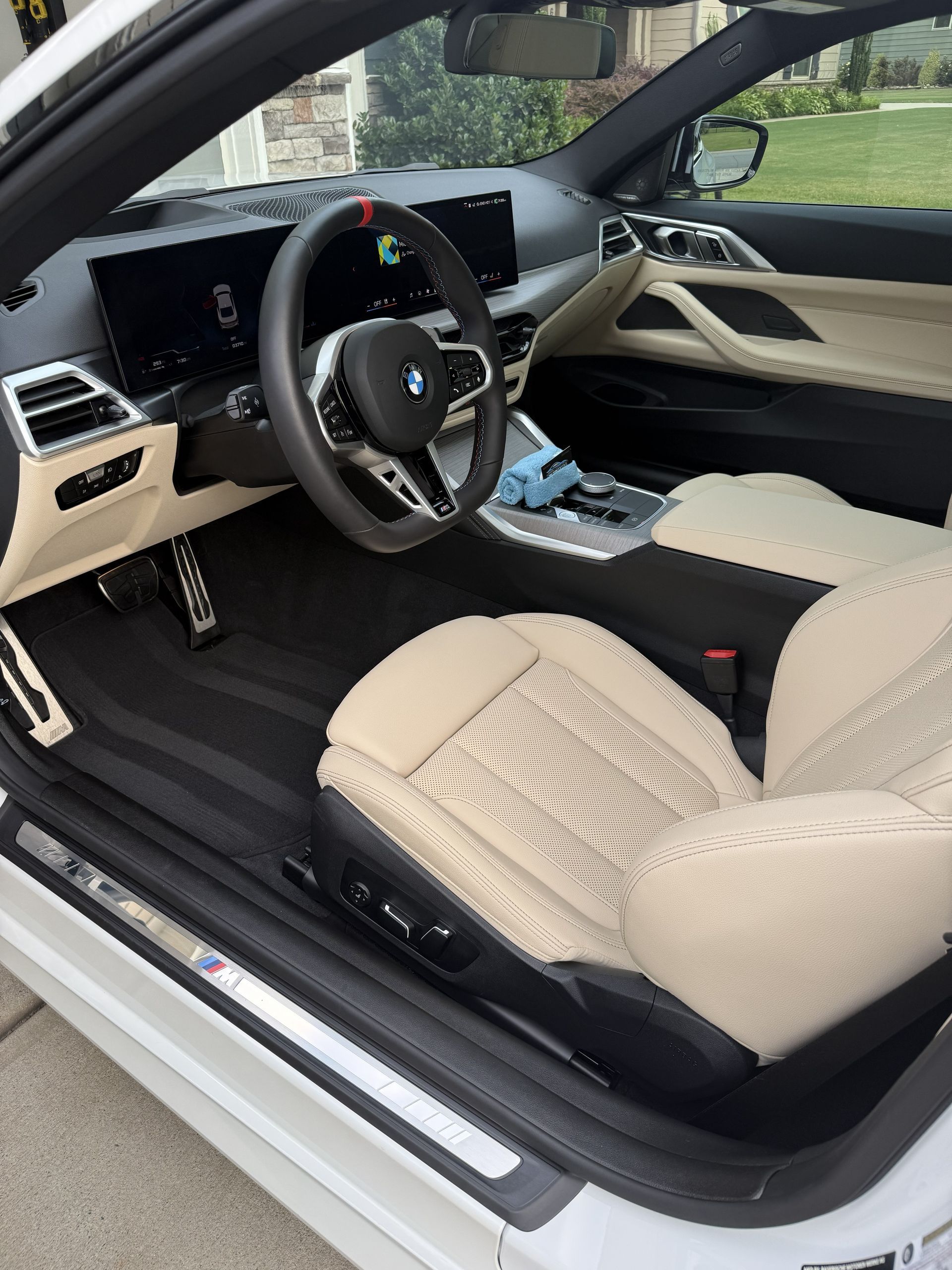 BMW interior with beige seats and dashboard, driver door open, showing steering wheel and center console