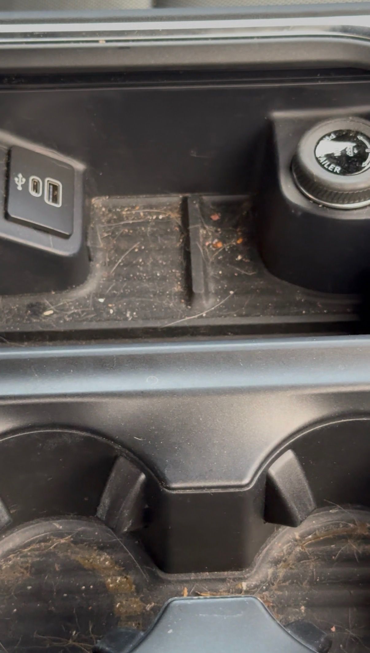 Close-up of a dusty car center console with two cup holders and a small dial.
