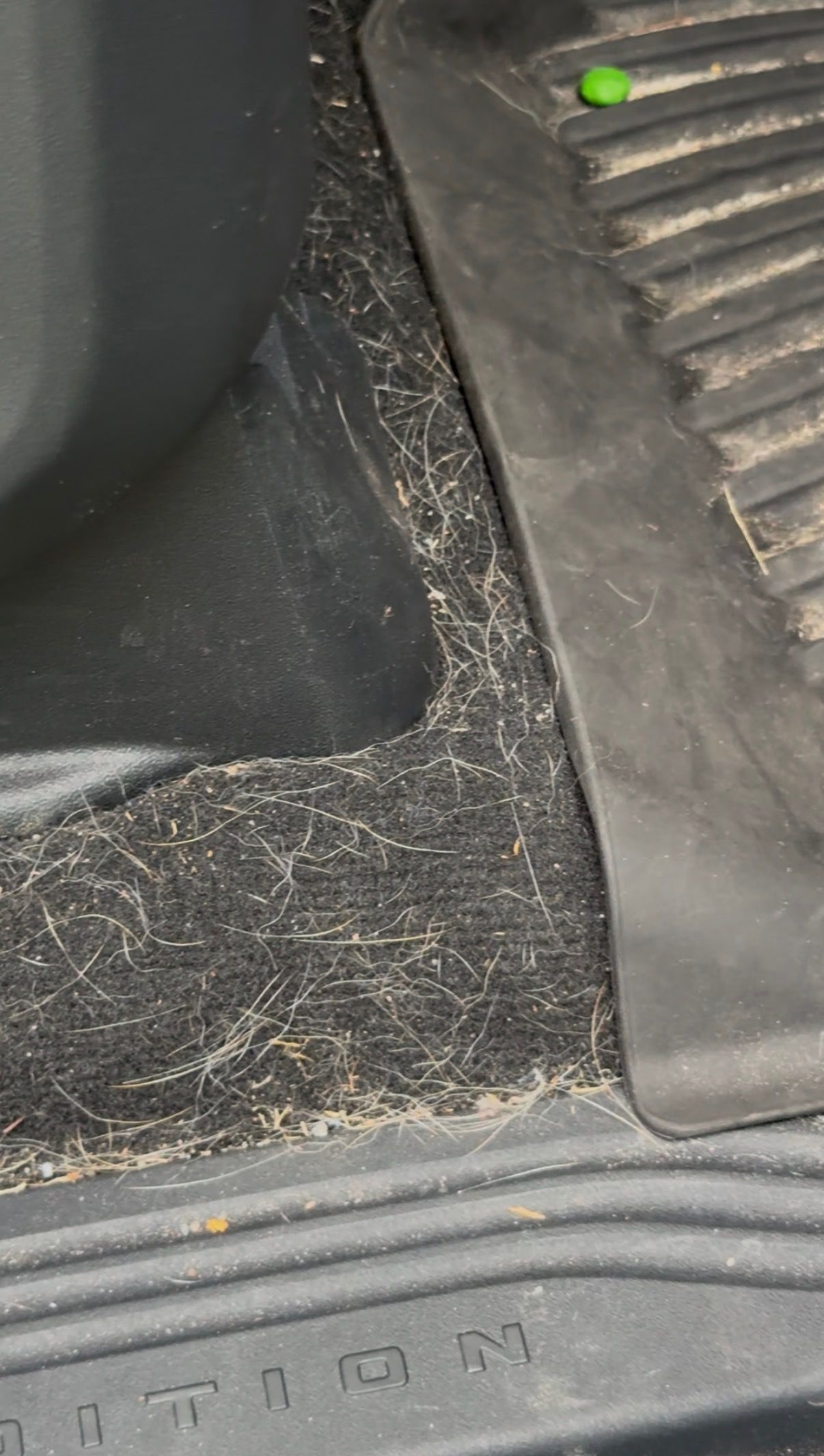 Dirty car floor mat with scattered debris and a green indicator light near the edge