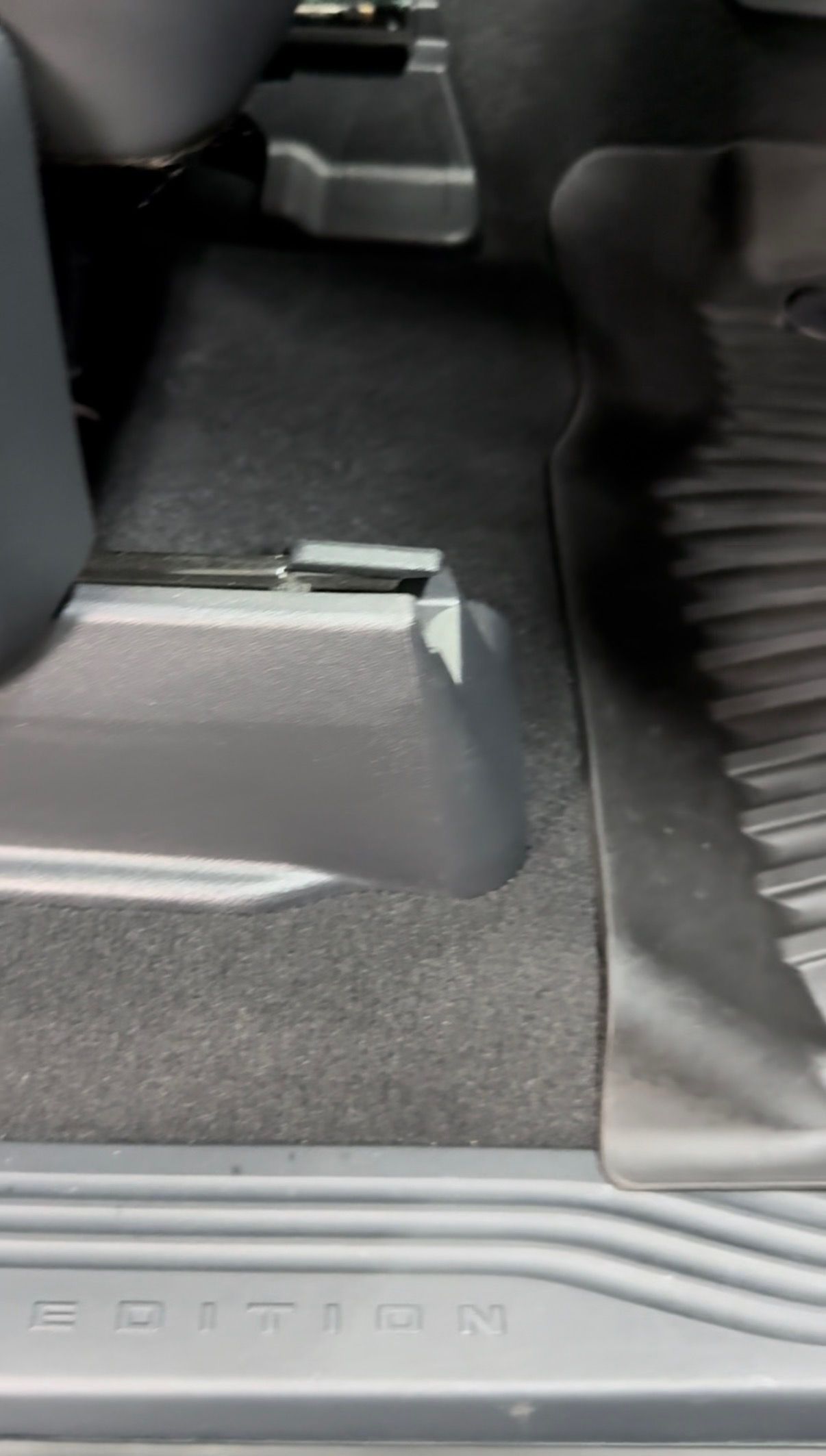 Car floor mat and seat base with black interior trim and a central console edge