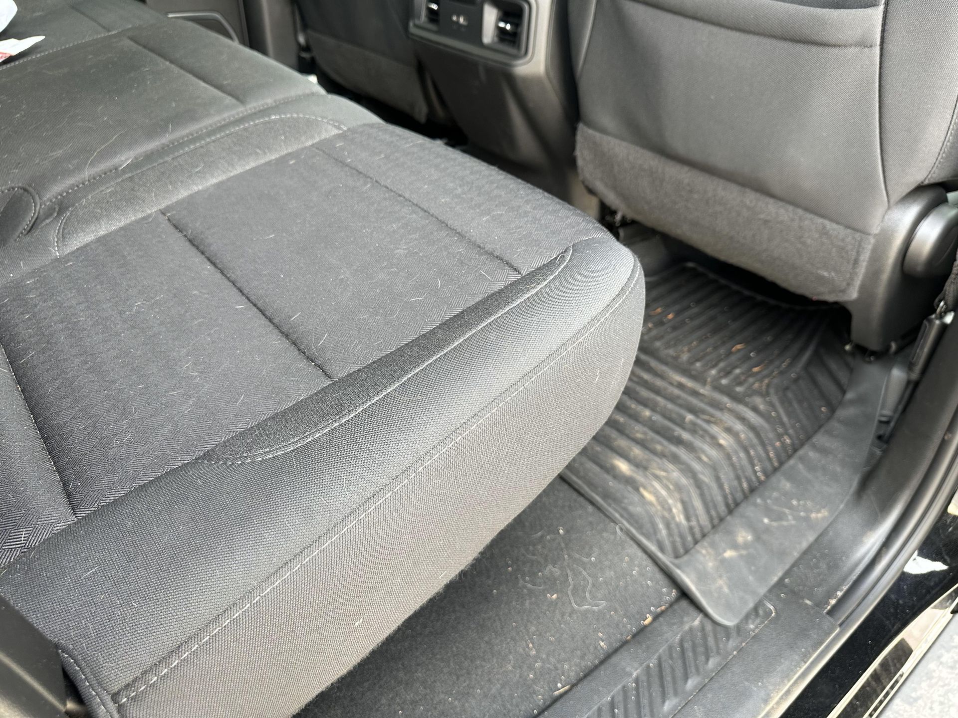 Black car back seat with floor mats, showing texture and some debris.