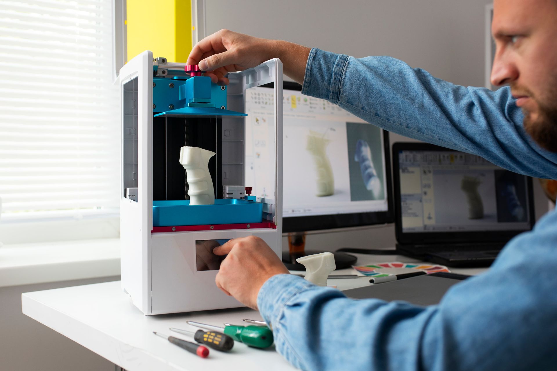 A man is working on a 3d printer at a desk.