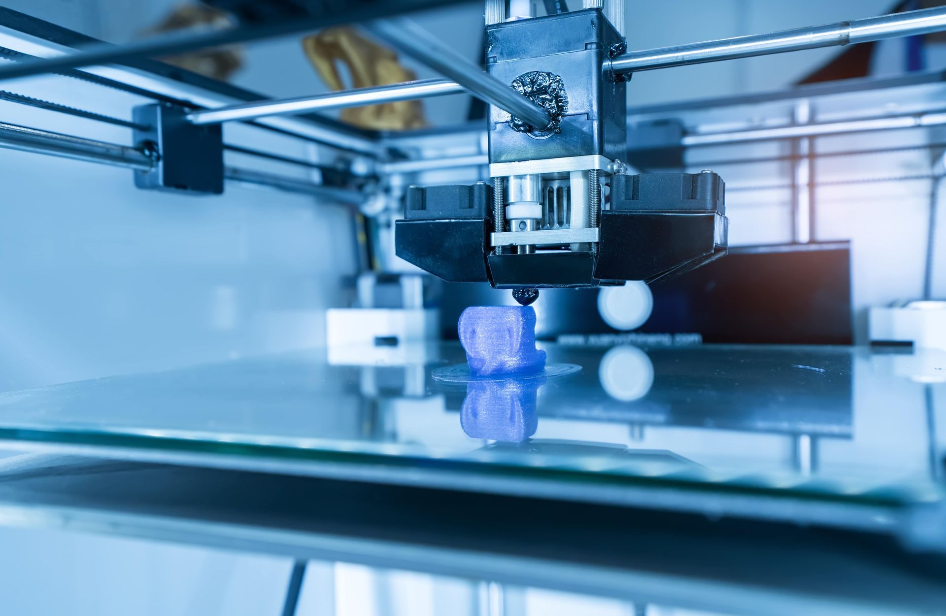 A 3d printer is printing a blue cube on a glass surface.