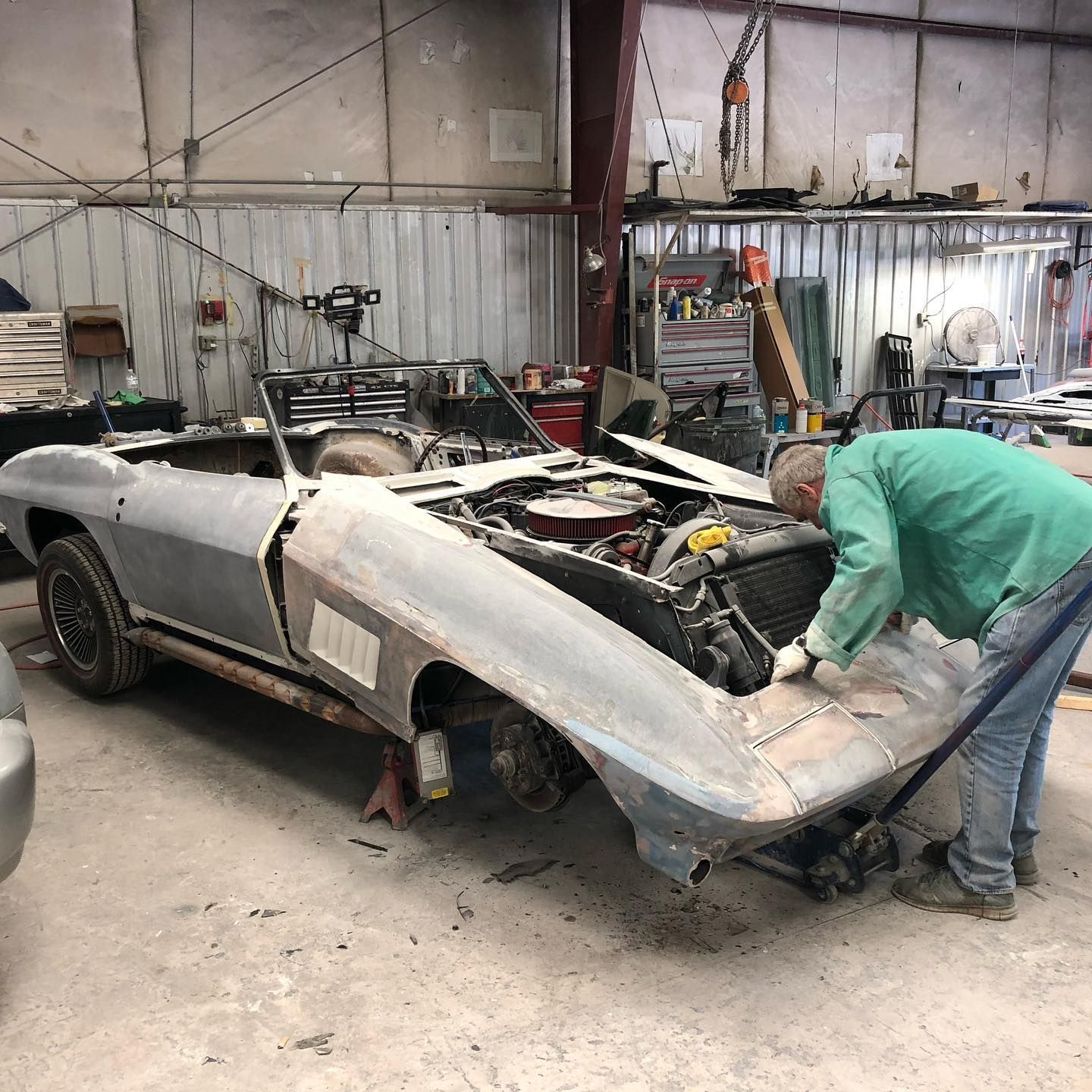 Man working on a classic convertible car in a garage, removing panels.