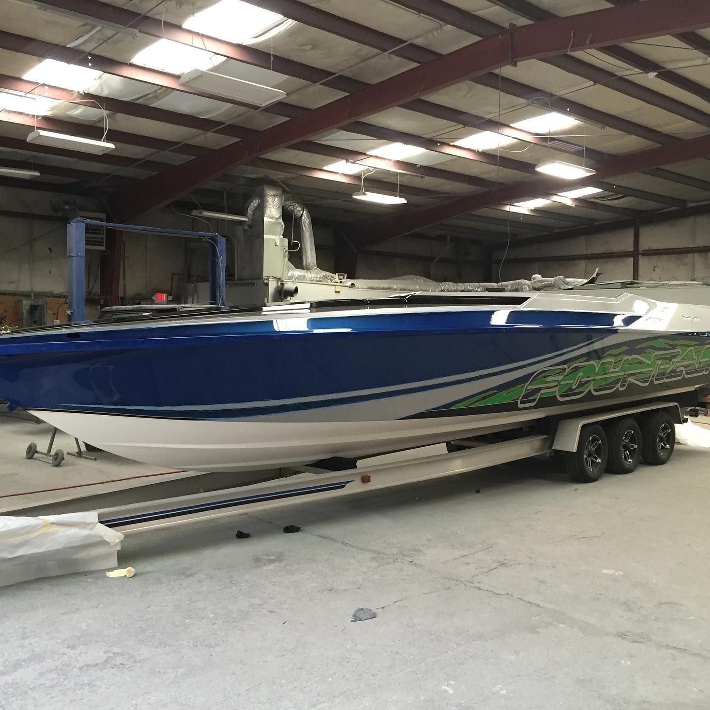 Blue and white speedboat with green accents, on a trailer inside a warehouse.
