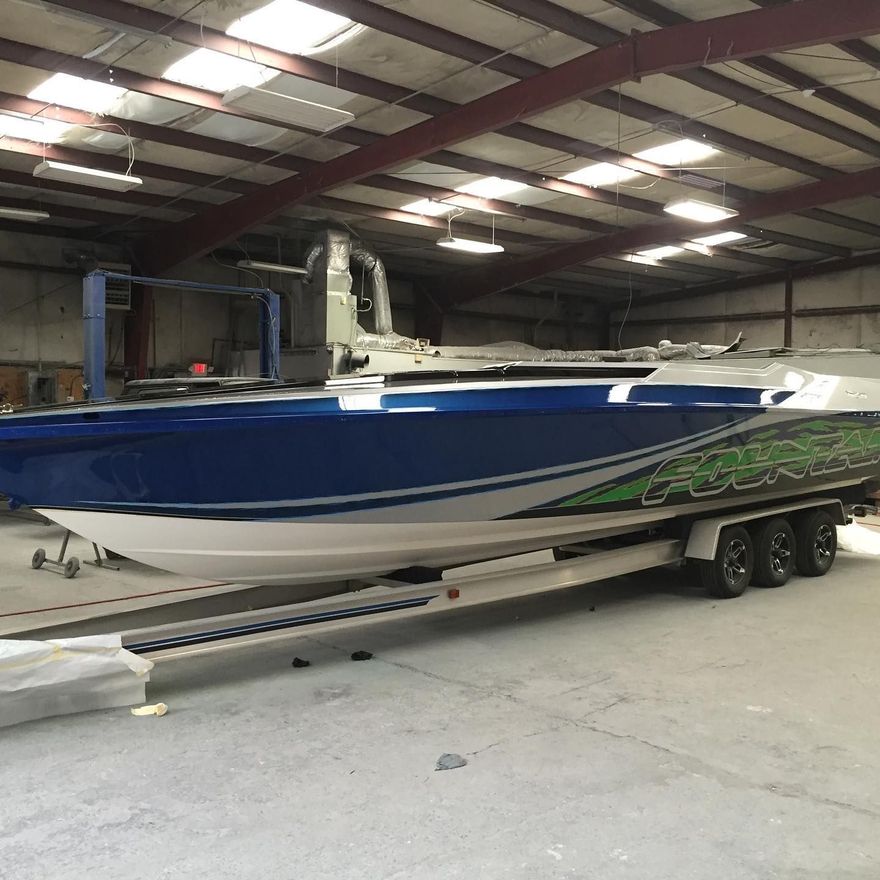 Blue and white speedboat with green accents, on a trailer inside a warehouse.