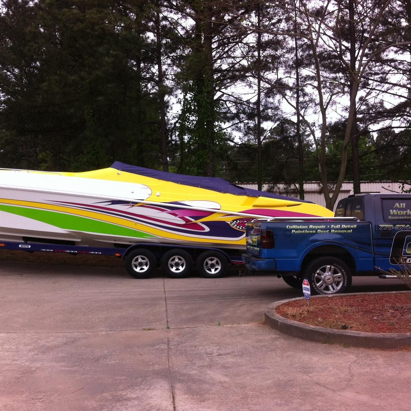 Brightly colored speedboat on a trailer hitched to a blue truck, parked outside.