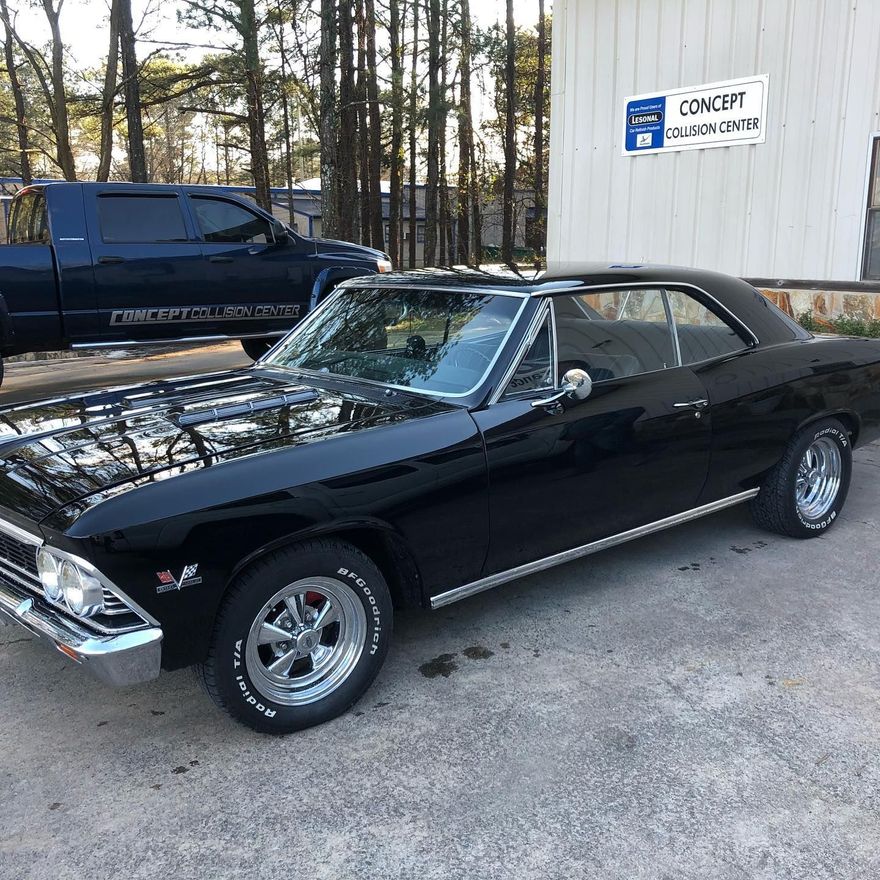 Black classic Chevrolet Chevelle parked outside a business, with a dark blue truck in the background.
